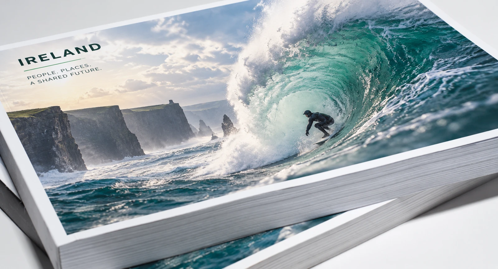 Illustrated Irish publication cover featuring a surfer in an Atlantic wave beside coastal cliffs, with the paper block visible