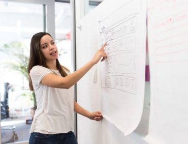 Women Wearing a white shirt standing beside a white board pointing at the board